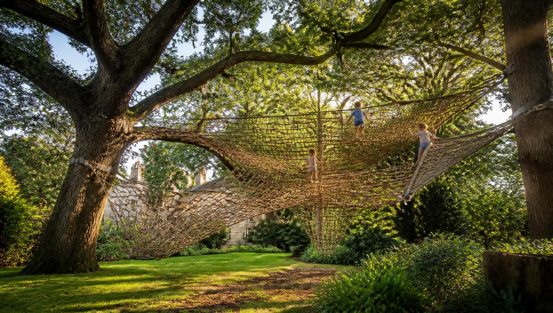 Large hand-woven TreeNet installation suspended between mature oak trees in a sunlit garden